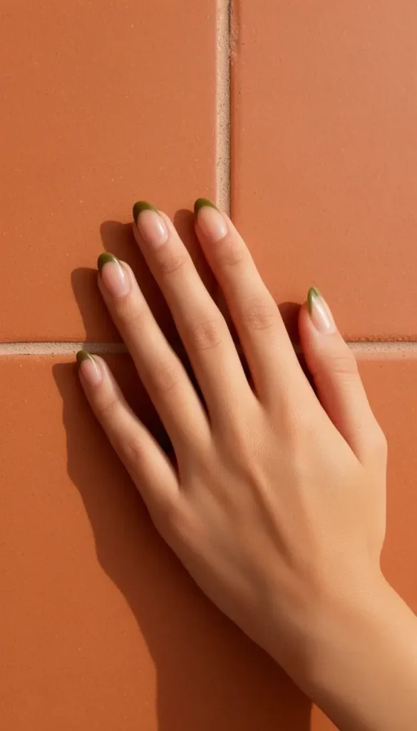 Olive-tipped French almond nails on a sheer nude base resting on terracotta ceramic tile.